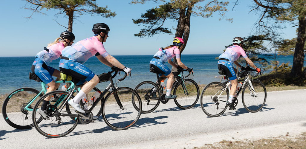 Fyra cyklister i färglada dräkter kör på en väg med ett vattendrag i bakgrunden