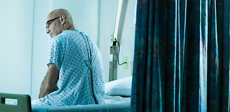 Man i sjukhuskläder sitter på en sjukhusäng