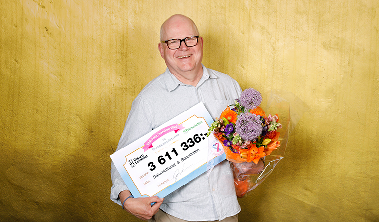 Olov Berggren med en check från Datumlotteriet i ena handen och en blomsterbukett i andra handen