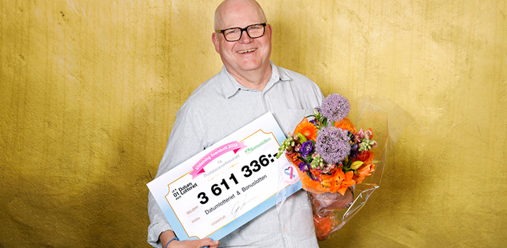 Olov Berggren med en check från Datumlotteriet i ena handen och en blomsterbukett i andra handen
