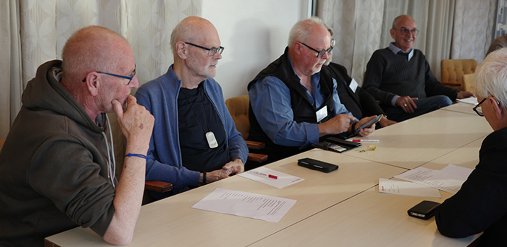 En grupp av äldre män sitter i en konferenslokal