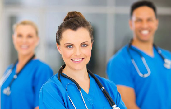 Två kvinnliga och en manlig sjuksköterskor i blåa arbetskläder