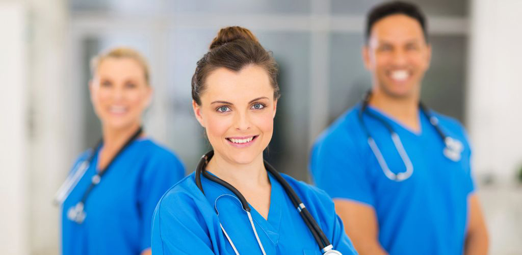 Två kvinnliga och en manlig sjuksköterskor i blåa arbetskläder