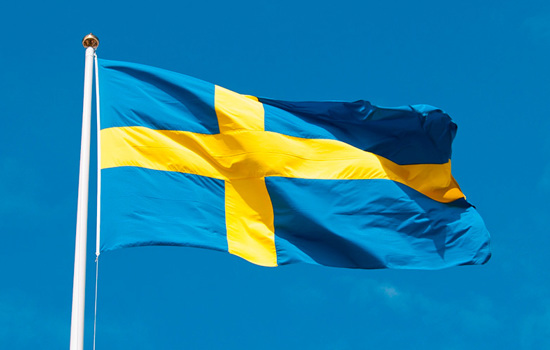 Sverigeflagga som vajar i vinden mot klarblå himmel