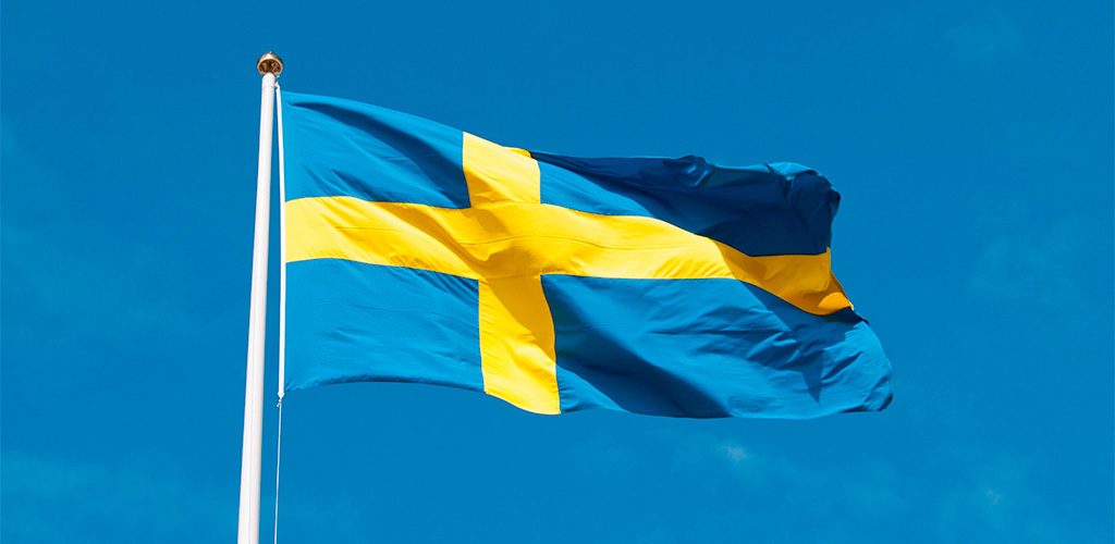 Sverigeflagga som vajar i vinden mot klarblå himmel