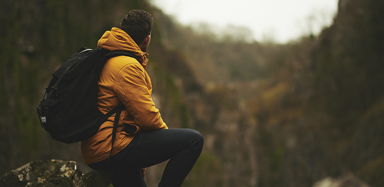 Man med en gul jacka och ryggsäck sitter på en sten i naturen